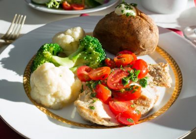 Baked potato, roast broccoli and cauliflower, tomatoes over chicken breast